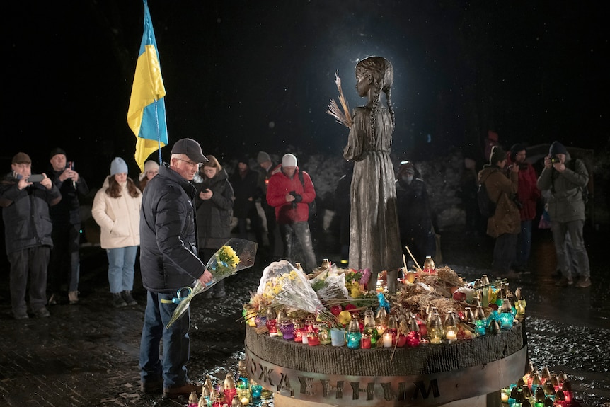 People light candles and lay flowers at a monument.