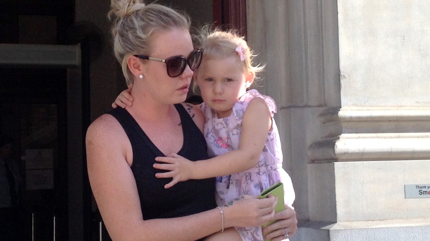 James Della's fiancé Kacey-Lee McWatters emerges from court holding their daughter in her arms.