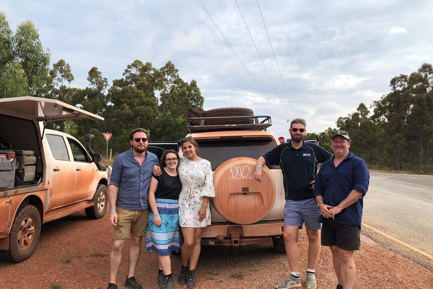Owain Stia-James and  ABC Darwin crew standing in front of car covered in red dust.