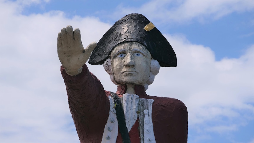 A large painted concrete statue of Captain Cook with his arm extended in front