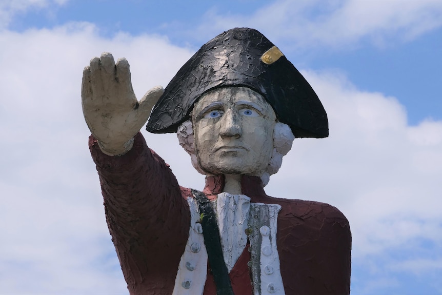 Une grande statue en béton peint du capitaine Cook, les bras tendus.