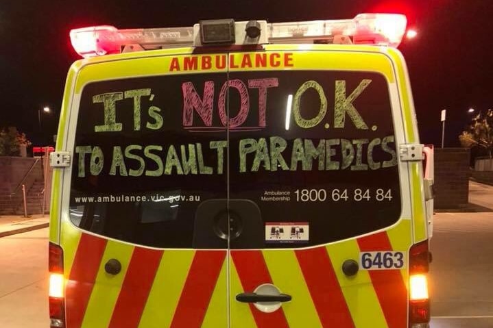 A handwritten sign that says 'It's not okay to assault paramedics" on the back of an ambulance.