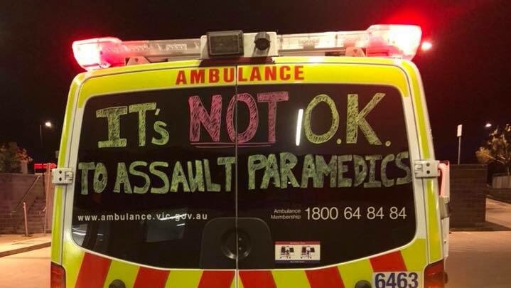 A handwritten sign that says 'It's not okay to assault paramedics" on the back of an ambulance.