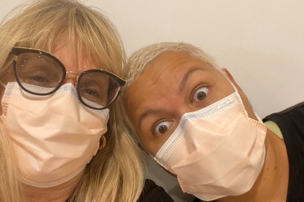 Two women wearing flu masks posing with their heads together