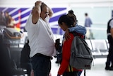 A man, holding his hands atop his head, and a woman looking down, arriving at an airport