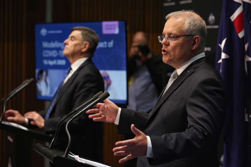 Scott Morrison in a suit and grey tie mid sentence standing next to the chief medical officer at a press conference.