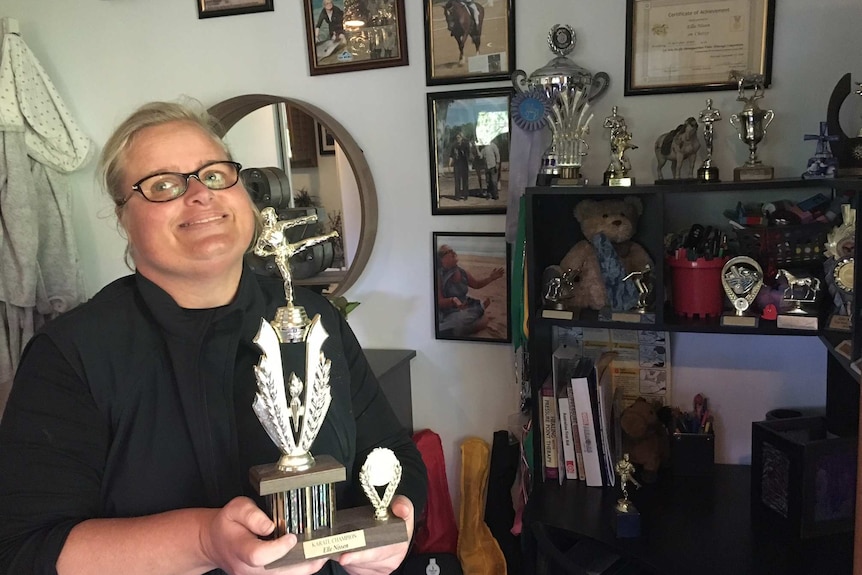 Eleka Nissen pose holding one of her karate trophies, with other trophies and certificates in the background