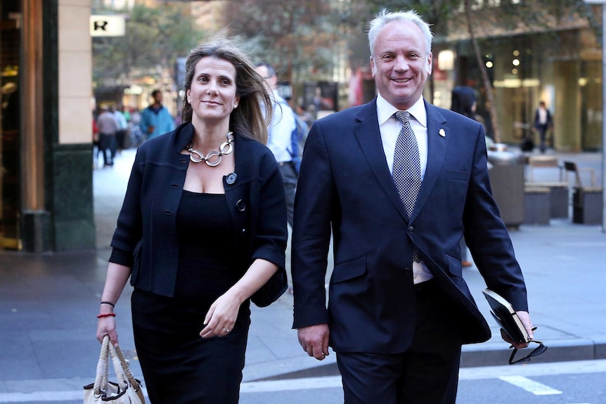 A man and a woman dressed in business clothing cross a street.