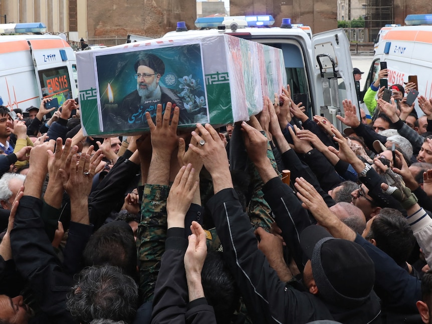 A crowd of people hold up a coffin decorated in Iranian flag with printed photo stuck to the side