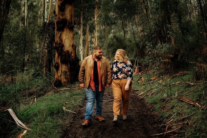 A man and woman holding hands with trees and bush in the background.