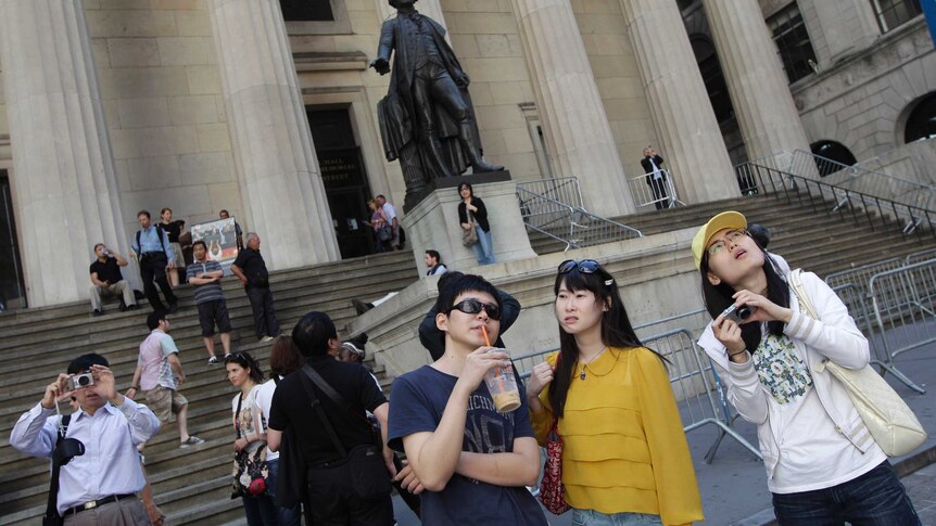 A group of tourists from China look around at the front of the New York Stock Exchange.