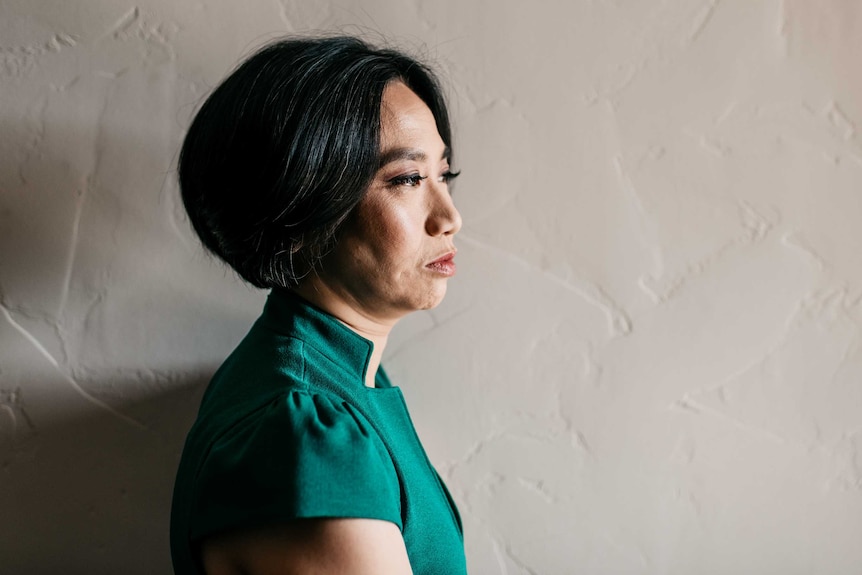 Rowena Chiu stands against a white wall wearing a green dress.