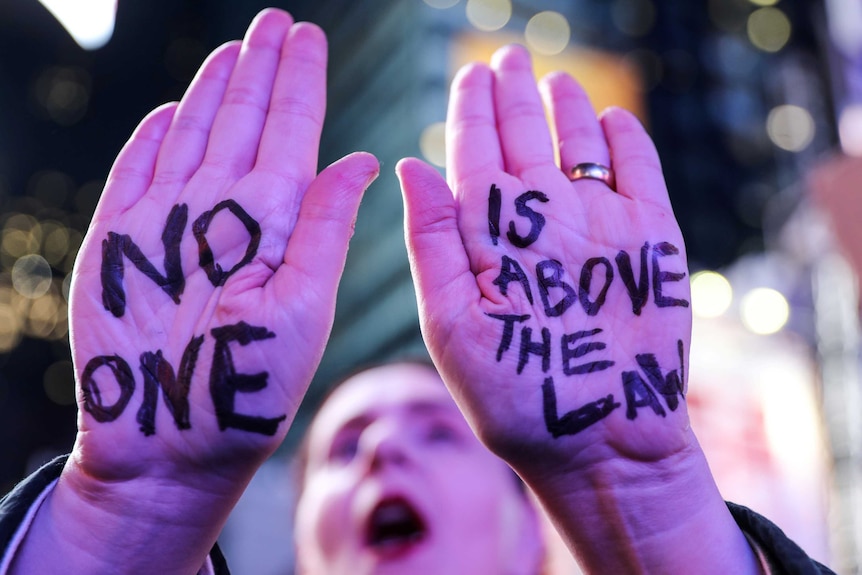 A protestor with "No One is Above the Law" written on their hands