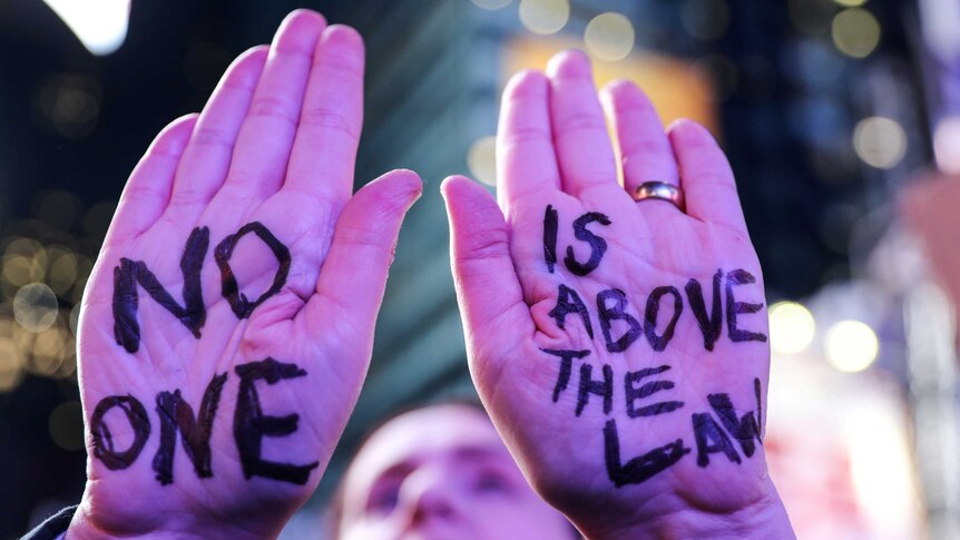 A protestor with "No One is Above the Law" written on their hands