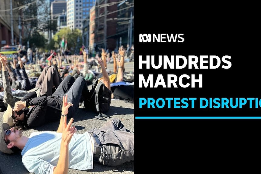 Hundreds March, Protest Disruption: Dozens of people lie on the ground razing their hands in the air.