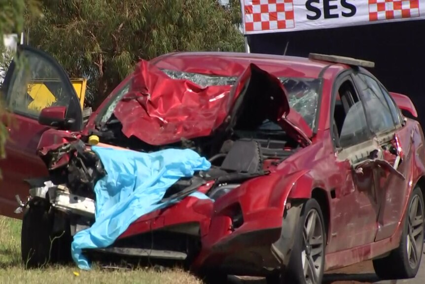 A red sedan is parked in front of an SES tent, its front comprehensively crushed and crumpled.