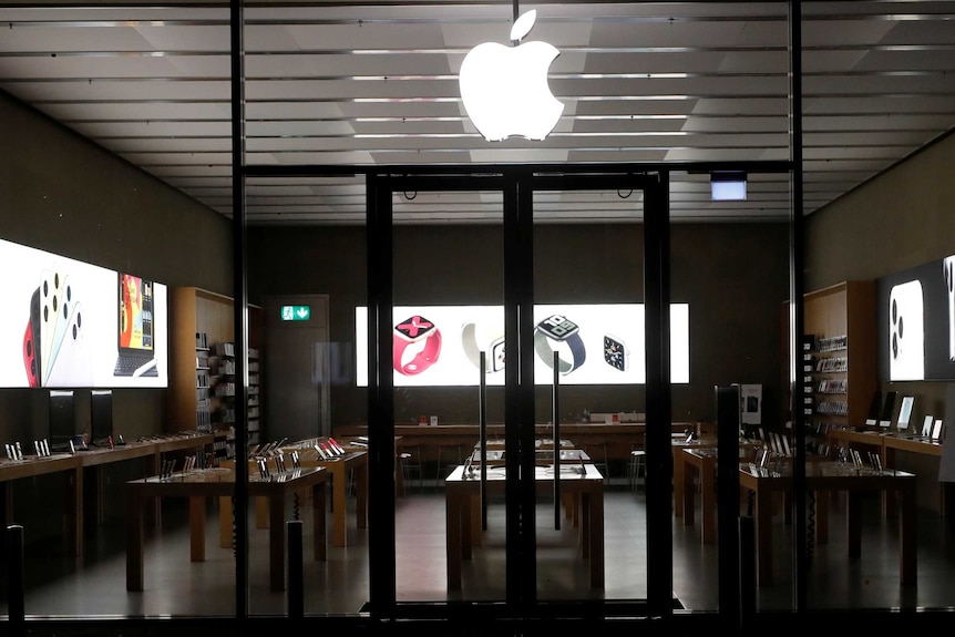 The logo of an apple on the front of a deserted electronics showroom with iPhones displayed inside