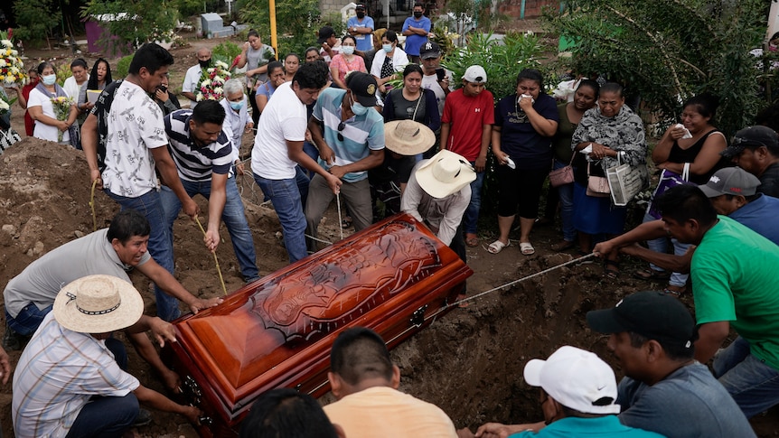 a dozen men lower a wooden, carved coffin with ropes into a grave