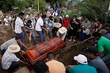 a dozen men lower a wooden, carved coffin with ropes into a grave