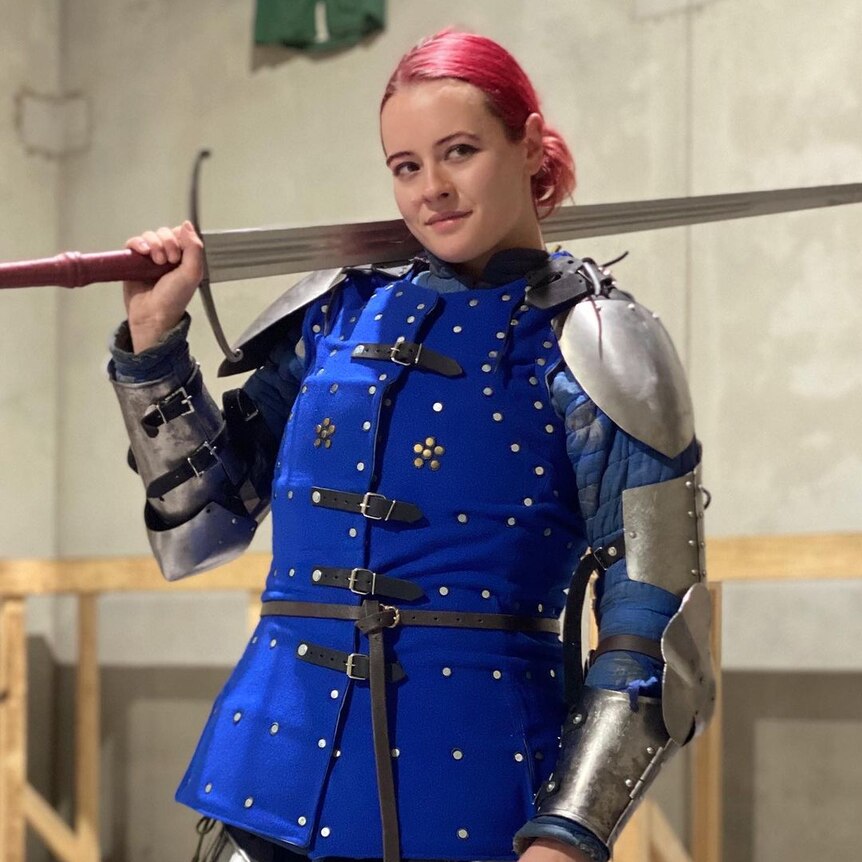 Molly Fry stands resplendent wearing a knight's armour with sword resting over one shoulder 