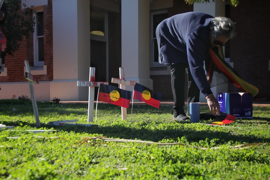 A woman places crosses in front of Geraldton Courthouse on the first day of the inquest into the death of JC.