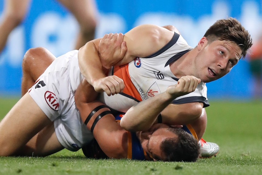 AFL player Toby Greene looks up as he presses his elbow to the face of a Brisbane player lying beneath him on the ground.