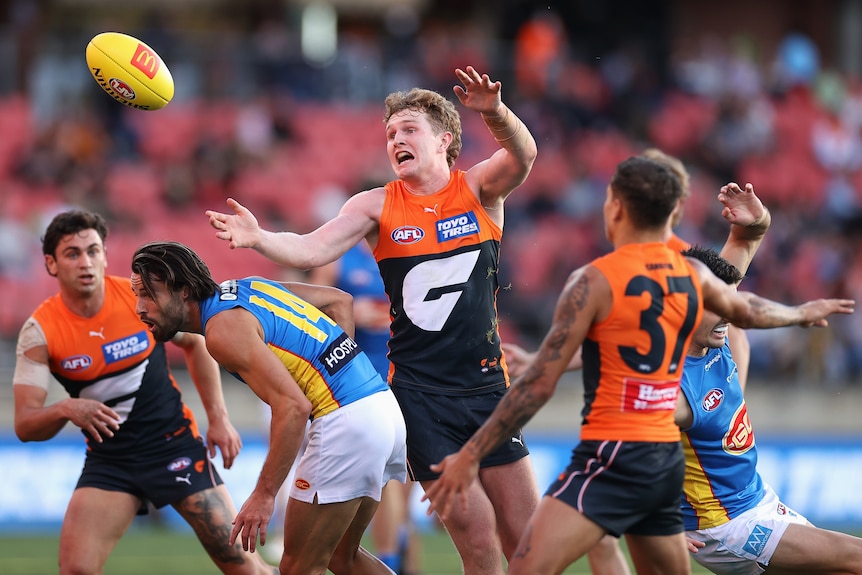 Tom Green holds his arms up as he reaches for the football in a pack of a number of Suns and Giants players