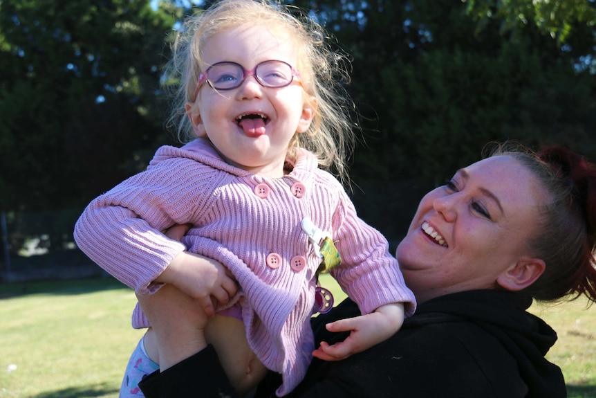 A mother lifts her two-year-old daughter in the air.