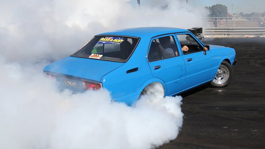 A blue car with smoke coming from its rear tyres as it does a drift.