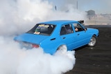 A blue car with smoke coming from its rear tyres as it does a drift.