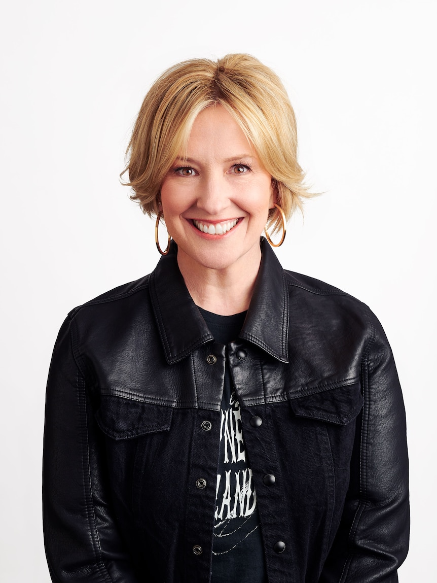 Blonde woman wearing black shirt and jacket smiling.