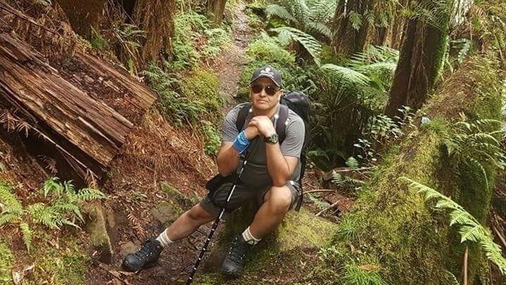 A male bushwalker rests on a rock on a track in a rainforest.