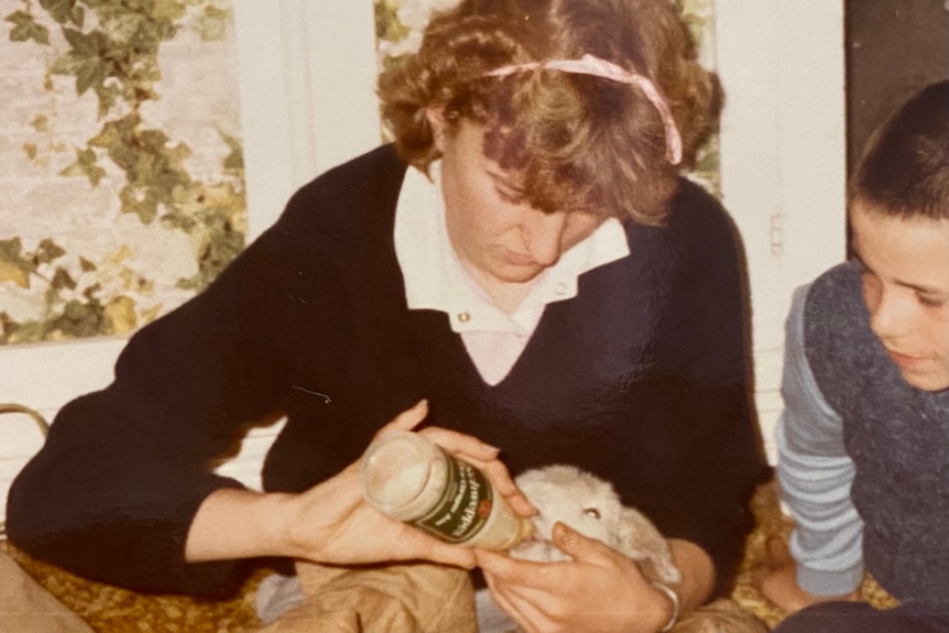 Old photo of teen girl feeding baby lamb