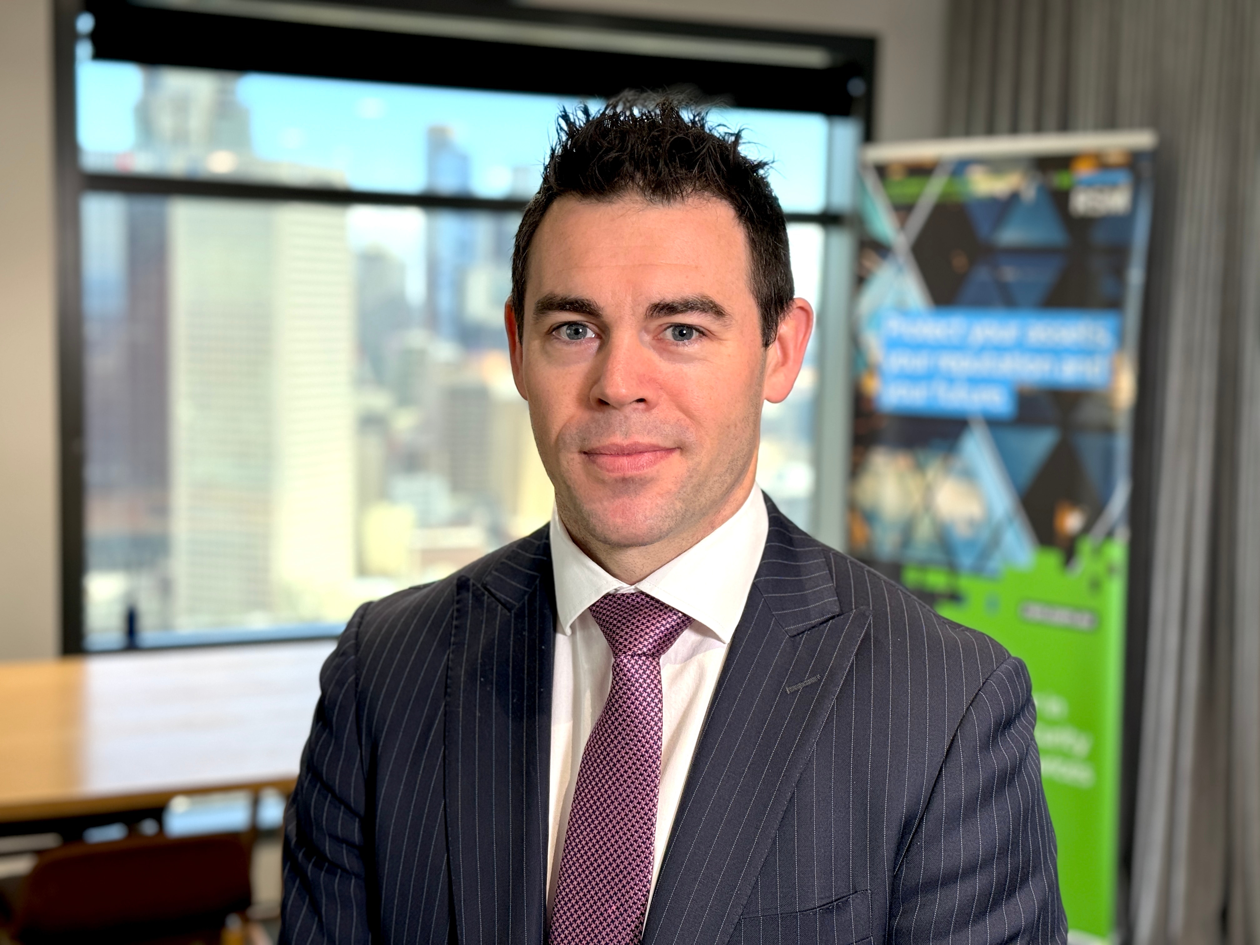 Man in suit looks at camera while standing in office with window. 