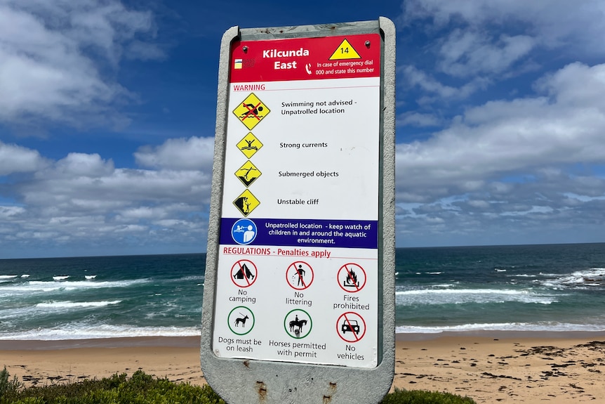 A sign in front of a beach outlining the rules to be followed in the area and advising people not to swim.