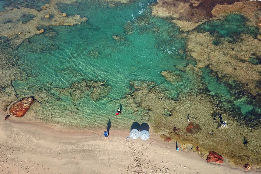 Drone shot of a rock pool in Kalbarri with beach umbrellas on the shore