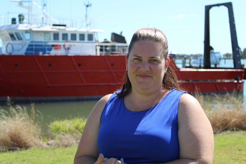 A woman in a blue shirt stands in the sun in front of a red ship