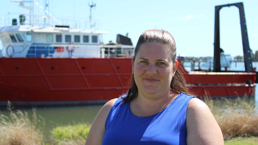 A woman in a blue shirt stands in the sun in front of a red ship