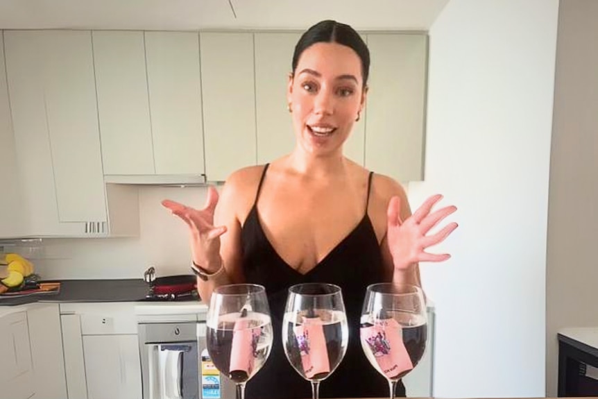 Jill Clarke stands in front of three glasses of water with pink vapes inside.