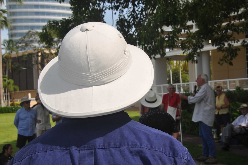 A man in a safari hat watching a speech