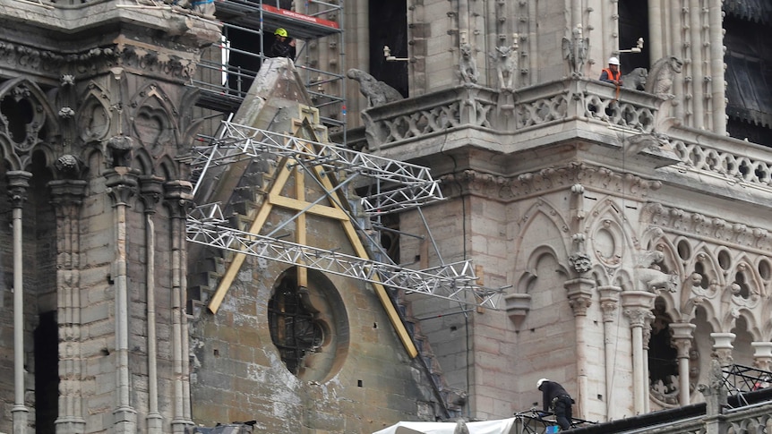 Workers in hardhats stand on scaffolding at the fire-ravaged Notre Dame to install tarps.