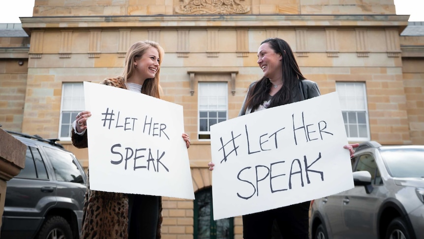 Two women with signs smiling at each other.