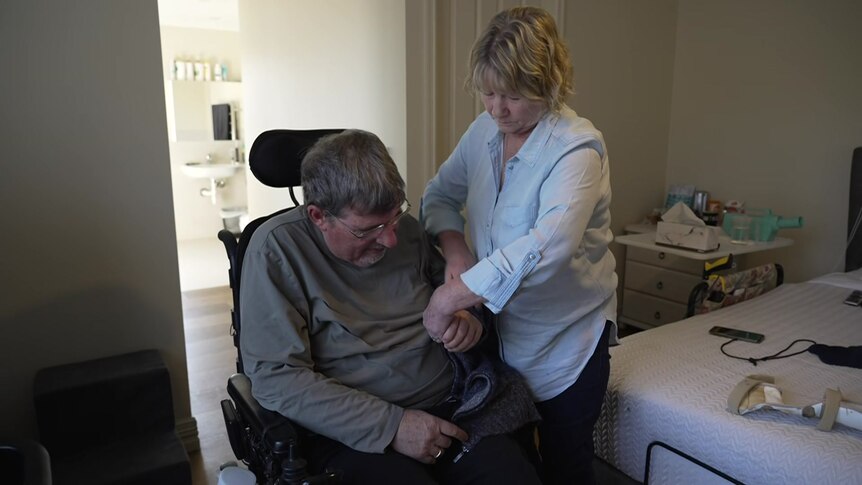 A woman holds the arm of a man sitting in a wheelchair.