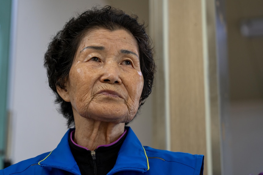 A close of an Asian woman wearing a blue jacket looking in the distance.