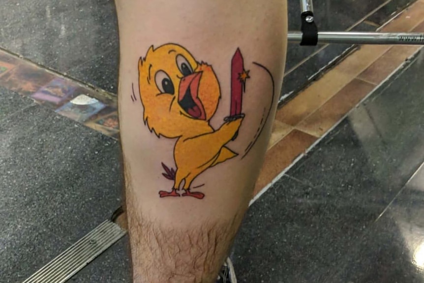 a man's calve showing a tattoo of a yellow chicken holding a red sword