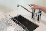 A woman's hand reaches out to turn off a kitchen tap. 