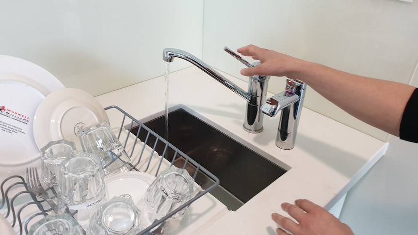 A woman's hand reaches out to turn off a kitchen tap. 