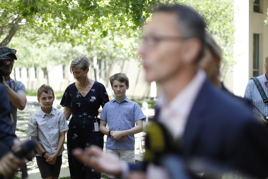 Lucy Quarterman puts her hands on her sons' backs as they watch Richard Di Natale address the media