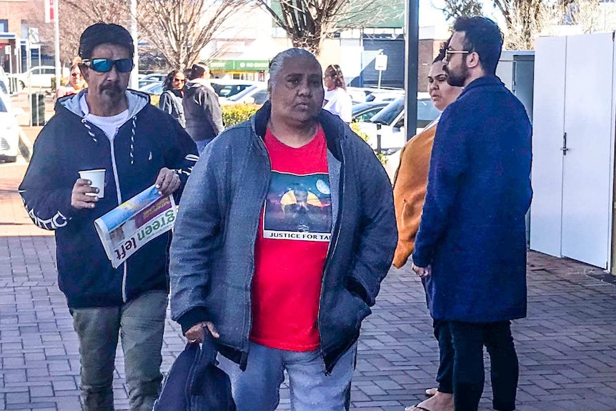 A man and a woman look solemnly at the camera while walking into court