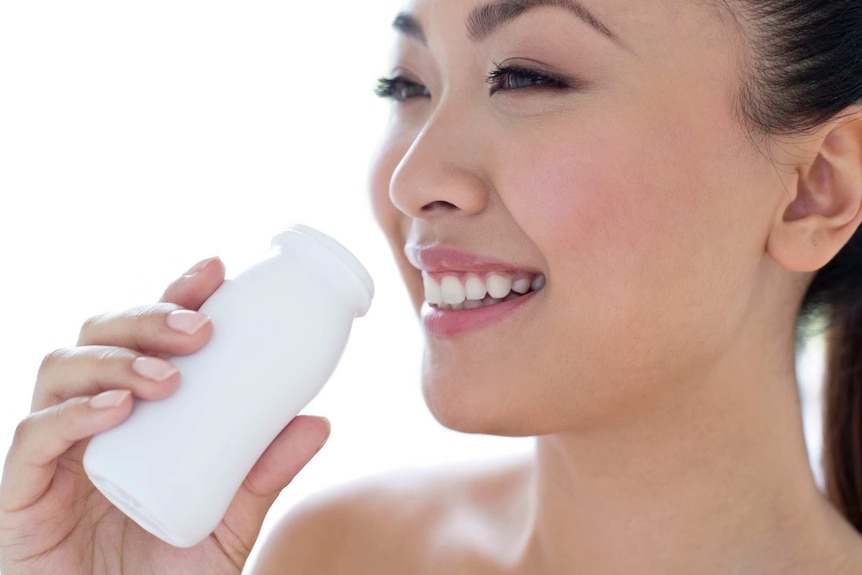 A woman smiles as she drinks a probiotic from a small bottle.